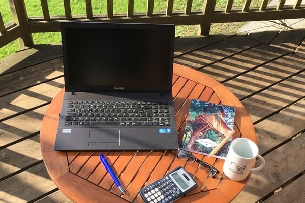 Laptop, Stifte, Brille und Kaffeetasse auf Tisch der Baumhausterrasse