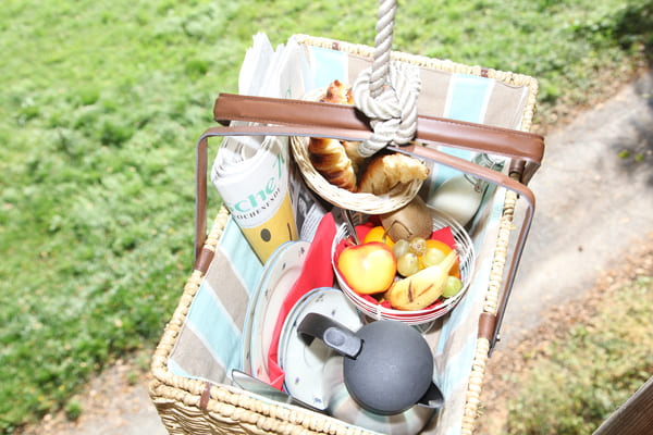 Frühstückskorb mit Obst, Gebäck, Kaffee, Geschirr, Milch und Zeitung am Seil