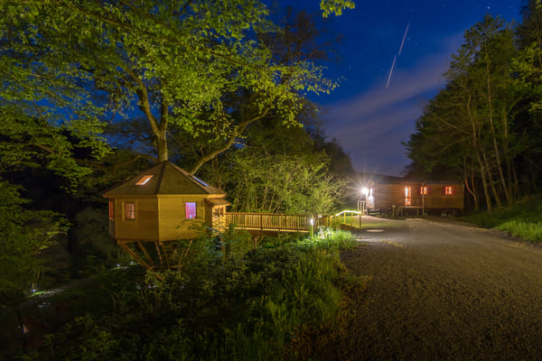 Sternenhimmel über einem beleuchteten Baumhaus und dem Schäferwagen